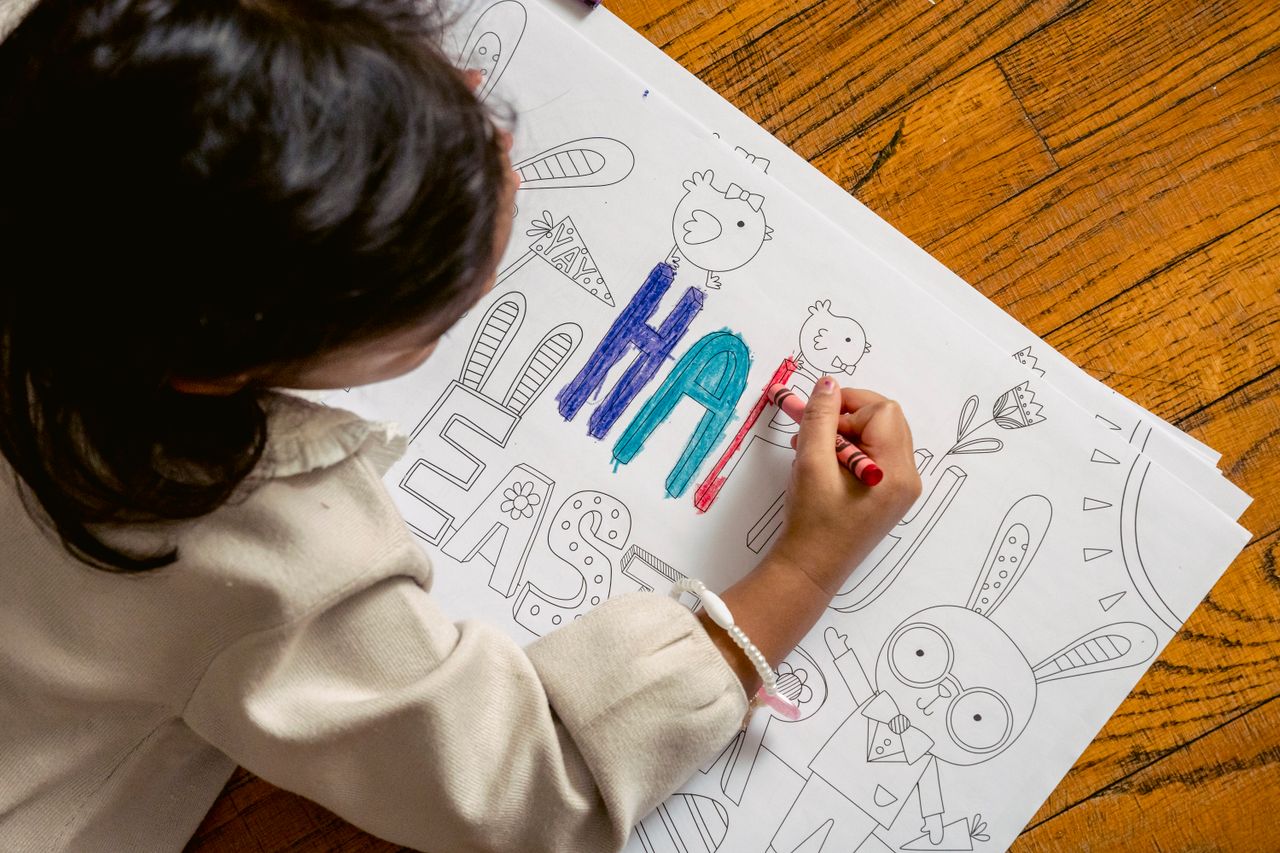 High angle back view of crop unrecognizable ethnic kid coloring Happy Easter inscription on drawing with crayon